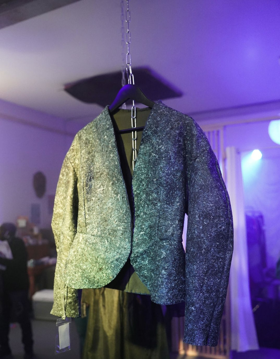 Collarless tailored jacket made from BioSpoke biomaterial, hung from a chain in a gallery